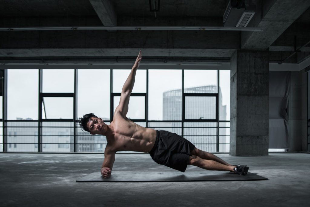 Homme faisant une planche latérale avec extension du bras opposé.