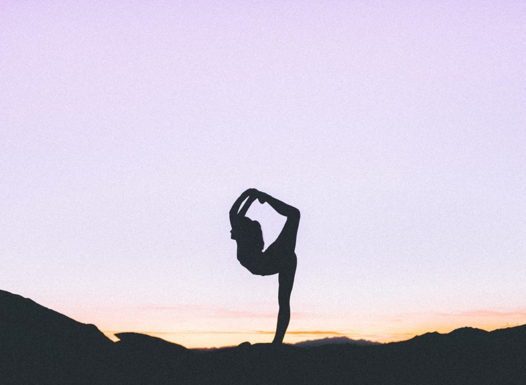 Ombre d'une femme faisant du yoga devant un ciel embrasé par le soleil couchant. 